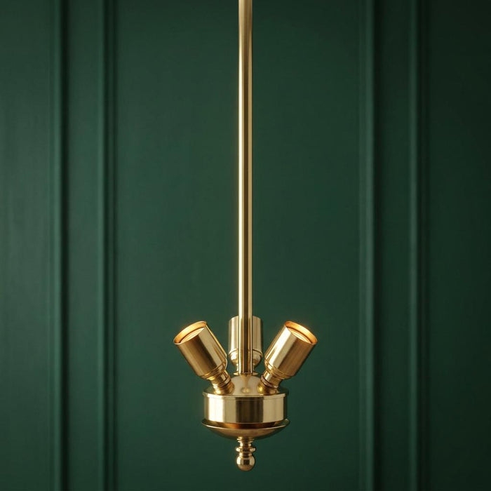 Polished brass 3-light suspension fitting with angled bulb holders against a dark green paneled wall.
