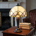 Abbey Tiffany table lamp with a floral cream glass shade and bronze base on a wooden side table with books.