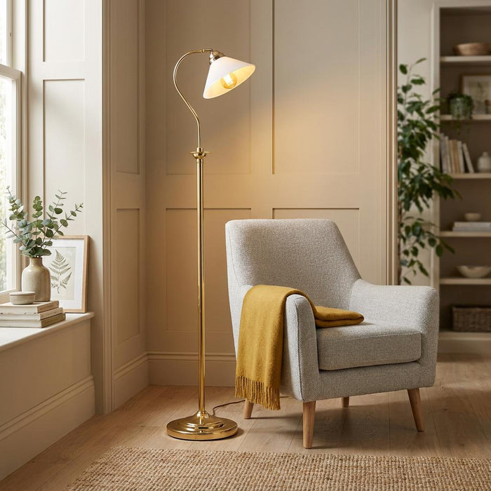 Adjustable antique brass floor lamp with a white glass shade illuminating a grey armchair in a cozy living room.