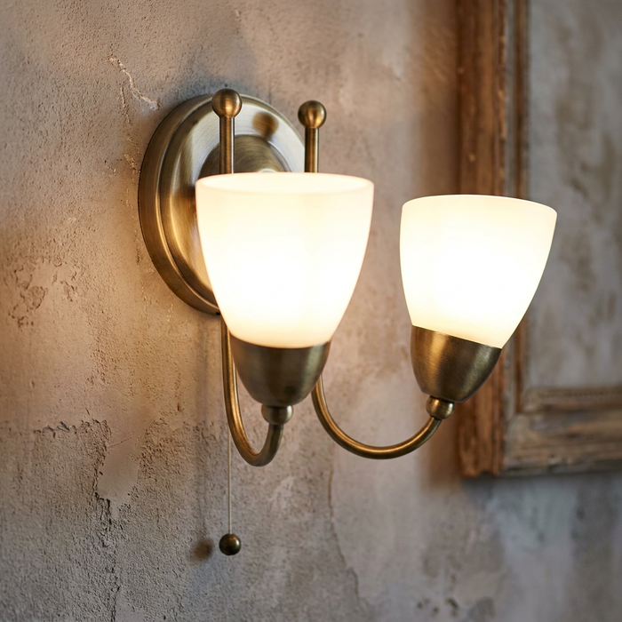 Altair double wall light in antique brass with glowing opal glass shades mounted on a textured wall.