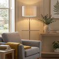 Altesse floor lamp with a wooden stand and oatmeal fabric shade in a warm, cozy living room setting.
