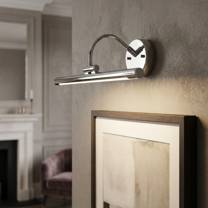 Polished chrome LED picture light mounted on a wall above a framed artwork in a living room.