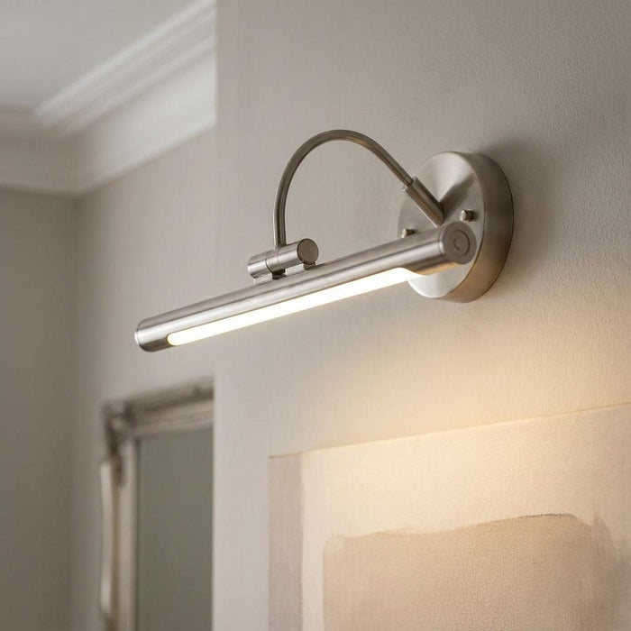 A sleek brushed nickel LED picture light mounted on a wall, casting a warm glow over a piece of artwork.