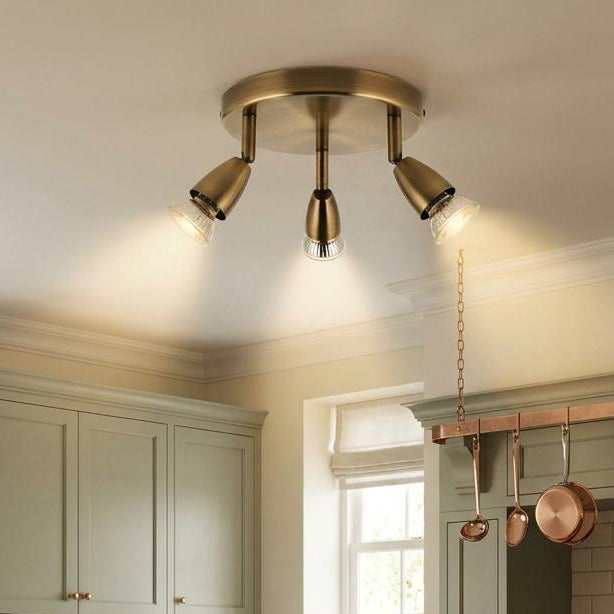 Amalfi 3 light antique brass ceiling spotlight illuminated in a kitchen with sage green cabinets and a wooden island.
