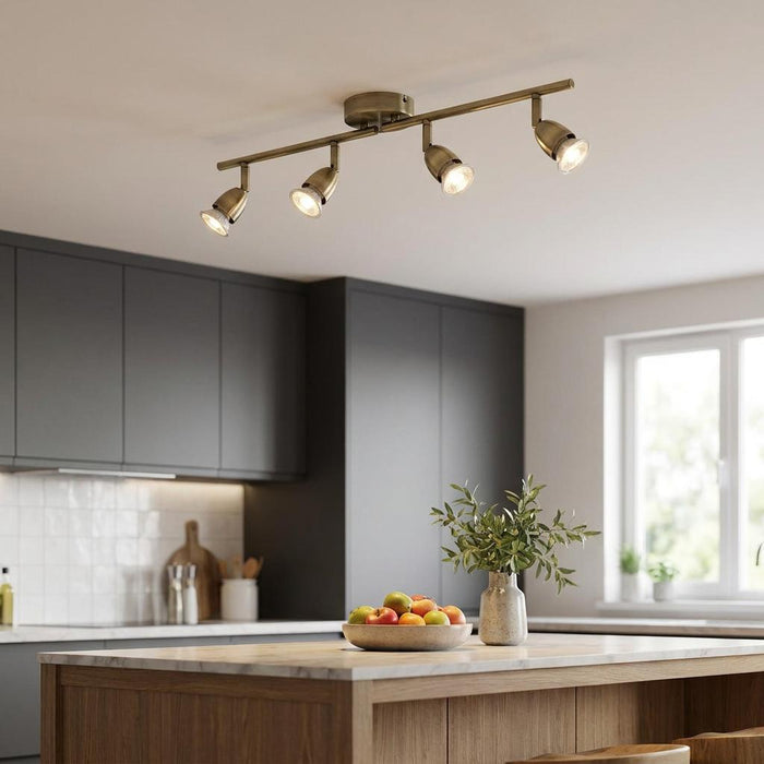 Four adjustable antique brass spotlights on a ceiling bar lighting a contemporary kitchen island.