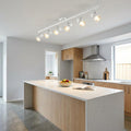 White Saxby Amalfi 6-light ceiling spotlight bar illuminating a modern kitchen island and light wood cabinetry.
