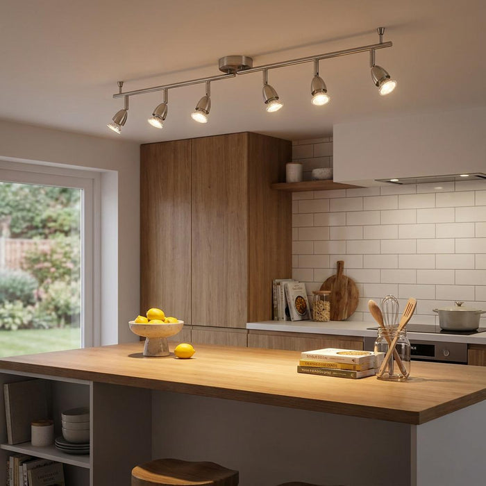 Six-light nickel bar spotlight illuminating a modern kitchen island with wooden cabinets and white tile backsplash.
