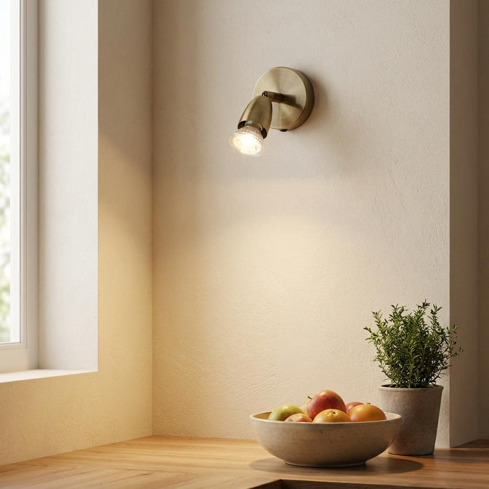 Amalfi Antique Brass Adjustable Spotlight mounted on a wall, illuminating a bowl of fruit on a wooden counter.