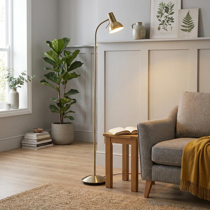 Amalfi antique brass floor lamp illuminating a cozy living room with a grey armchair and potted plant.