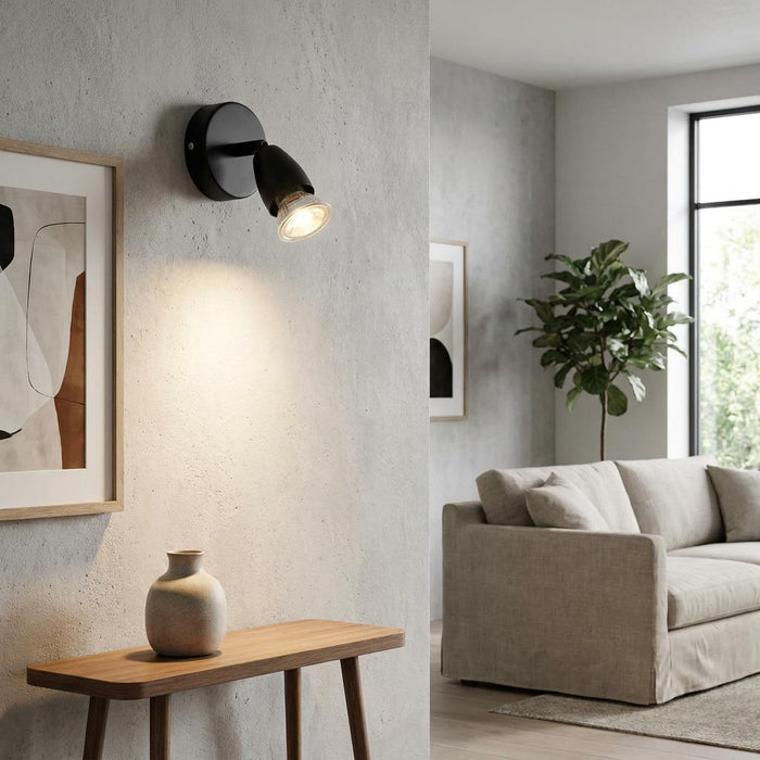 Black adjustable wall spotlight illuminates a textured wall above a wooden console in a minimalist living room.