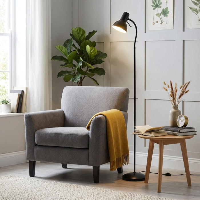 Amalfi black reading floor lamp standing next to a grey armchair with a yellow throw in a bright living room.