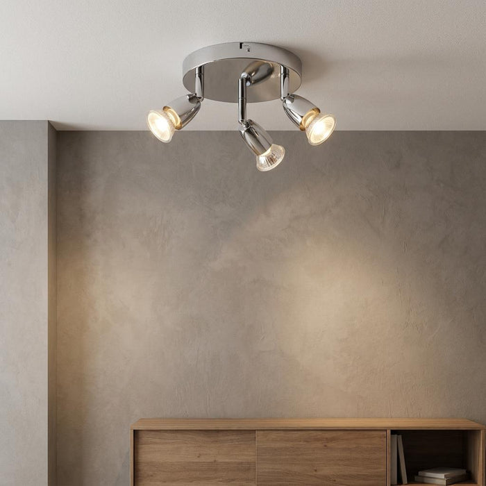 Saxby Amalfi chrome 3-light spotlight fixture illuminating a textured gray wall above a wooden sideboard.