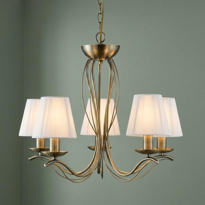 Andretti 5-light brass chandelier with glowing cream string shades and elegant curved arms against a green wall.