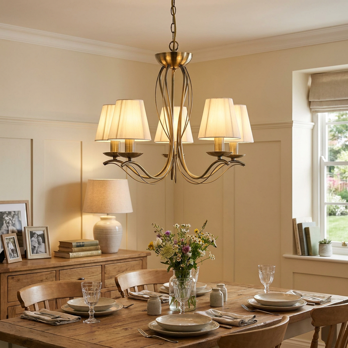 A brass 5-light chandelier with cream string shades illuminates an elegantly set wooden dining table.