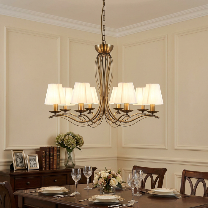 Eight-light antique brass chandelier with cream shades over a set dining table in a paneled room.