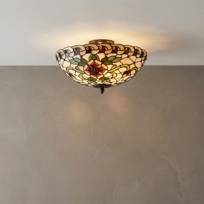 Angelique large semi flush Tiffany ceiling light with floral stained glass shade glowing on a white ceiling.