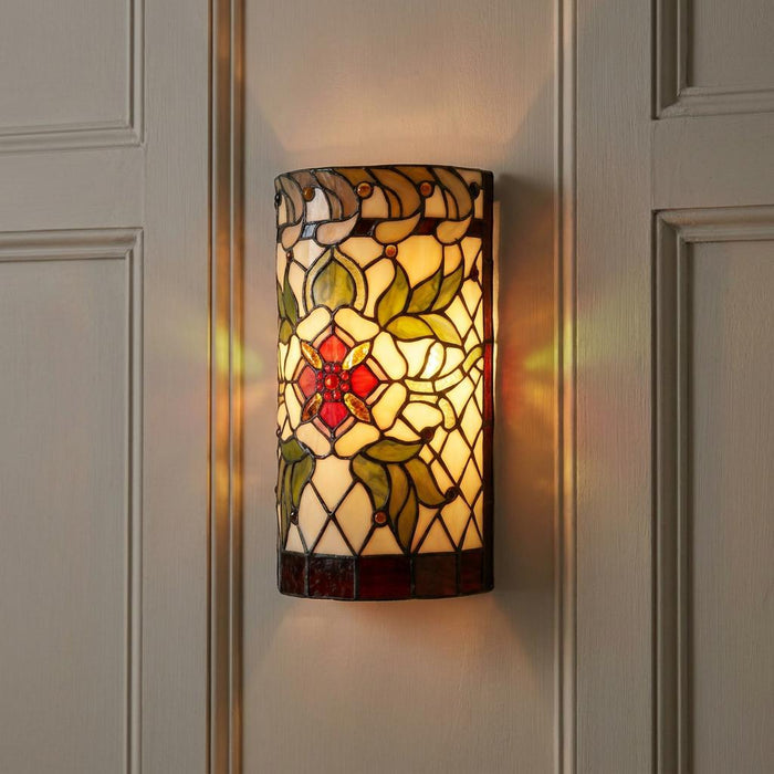 Illuminated Tiffany-style floral wall sconce with red and green stained glass mounted on a white paneled wall.
