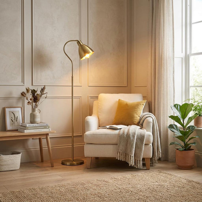 Antique brass floor lamp with a curved arm illuminates a cozy reading nook with a cream armchair.