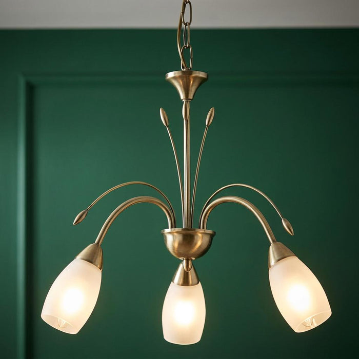 Antwerp 3 light antique brass chandelier with frosted glass shades against a dark green paneled wall.