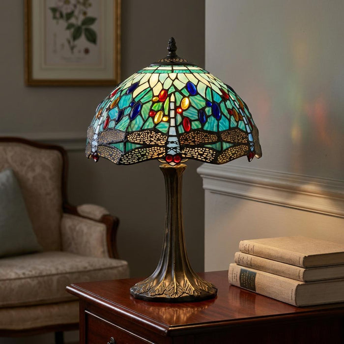Aqua Tiffany table lamp with dragonfly stained glass shade on a wooden side table next to vintage books.