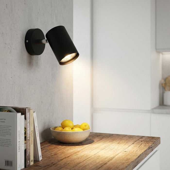 Matte black adjustable wall spotlight illuminating a wooden counter with a bowl of lemons in a modern kitchen.