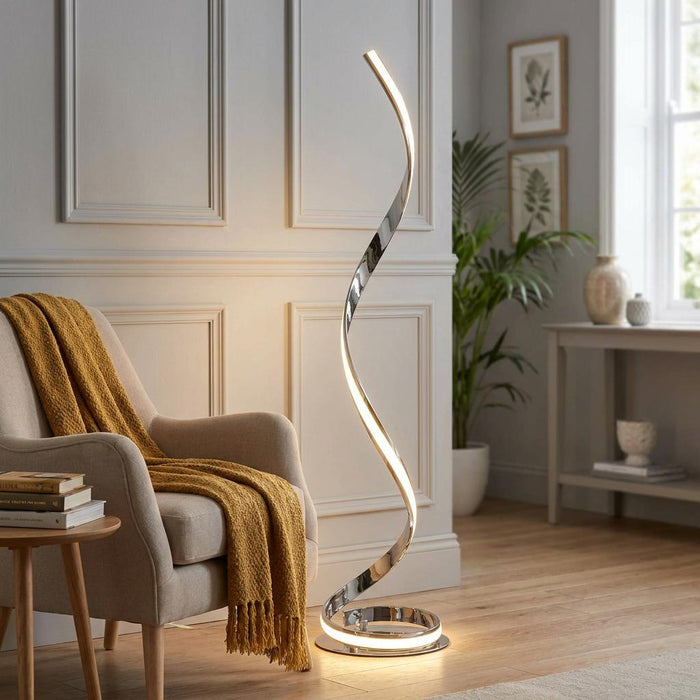 Modern chrome spiral LED floor lamp illuminates a cozy living room next to a beige armchair with a yellow throw.