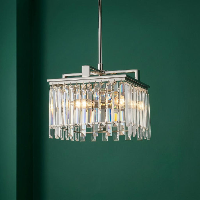 Small polished nickel chandelier with rectangular crystal prisms, illuminated against a deep green wall.