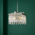 Small polished nickel chandelier with rectangular crystal prisms, illuminated against a deep green wall.