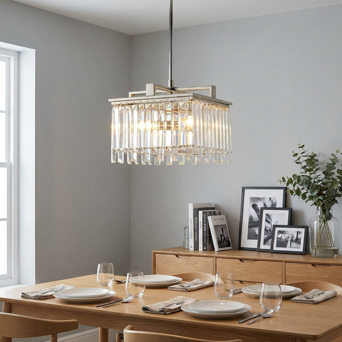 Polished nickel square chandelier with vertical glass crystals hanging over a minimalist dining table setting.