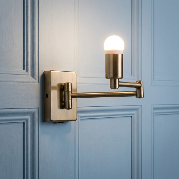 Armada antique brass double swing arm wall lamp with a glowing bulb mounted on a light blue paneled wall.