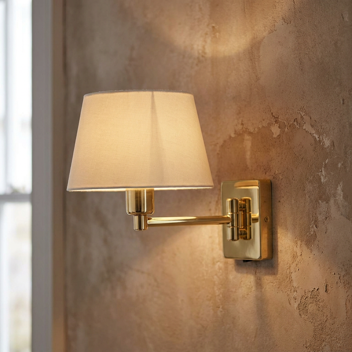 Armada polished brass single swing arm wall light with a cream fabric shade mounted on a textured wall.