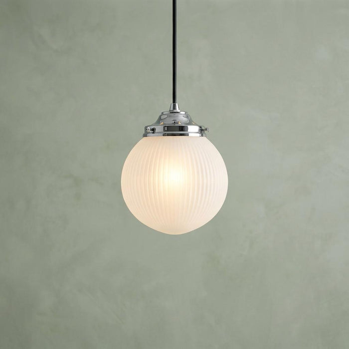 Chrome pendant light with a glowing, frosted ribbed glass globe against a textured green wall.