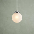 Chrome pendant light with a glowing, frosted ribbed glass globe against a textured green wall.