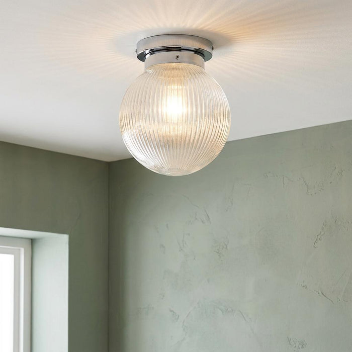 Art Deco prismatic glass globe flush ceiling light with a chrome base, casting a radial glow on a white ceiling.
