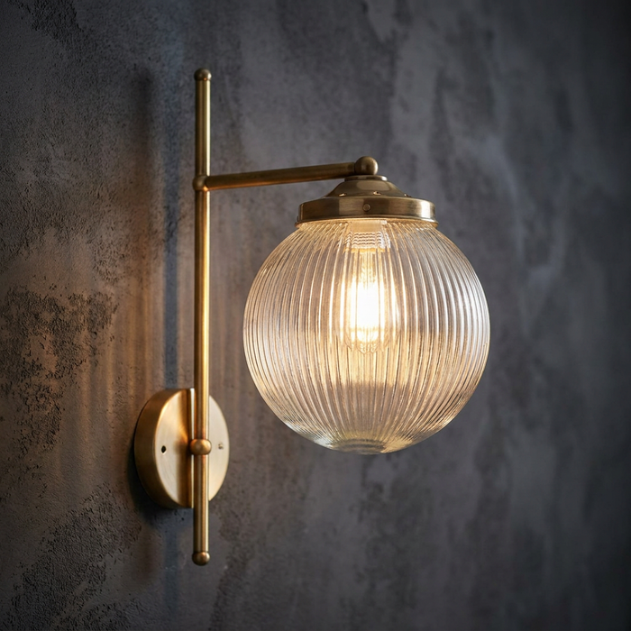 Art Deco wall light with a ribbed glass globe and brass arm mounted on a dark textured wall.
