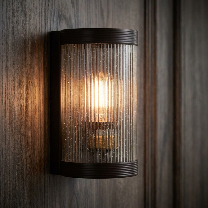 An illuminated Art Deco reeded glass wall light with a dark bronze finish, mounted on a dark wood-paneled wall.