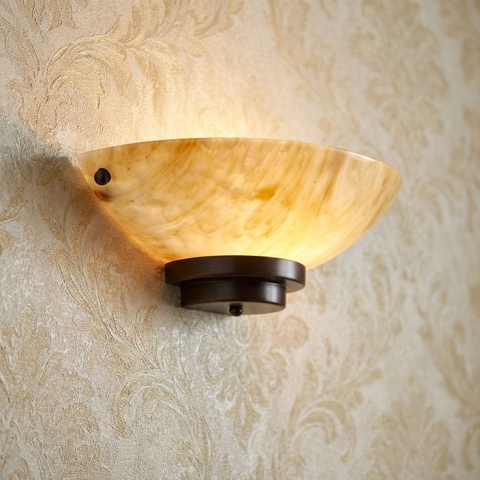 Alabaster glass bowl wall sconce with a dark bronze base mounted on beige damask wallpaper.