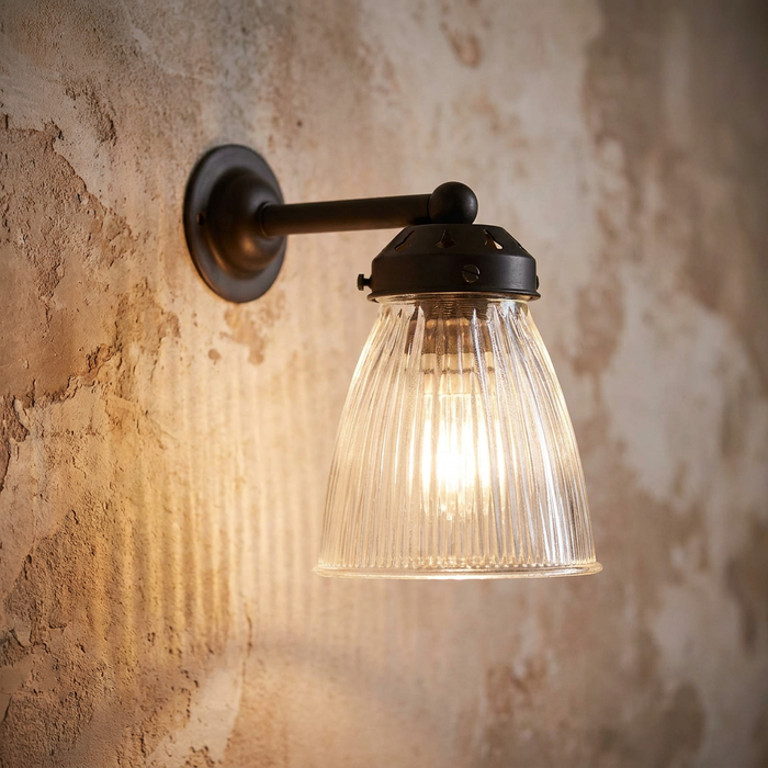 Lit Art Deco wall light with a fluted glass shade and dark bronze arm mounted on a rustic plaster wall.