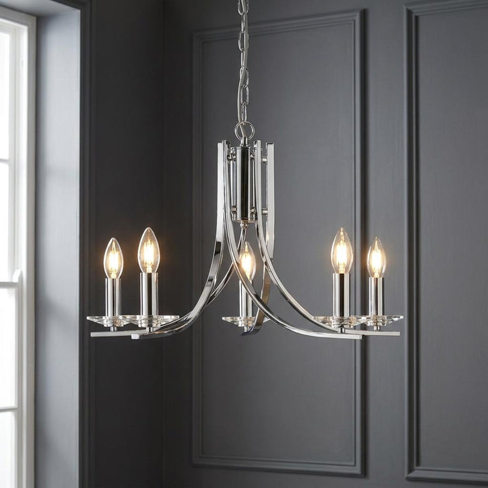 Modern five-light chrome chandelier with glass sconces and candle bulbs against a dark grey wood-panelled wall.