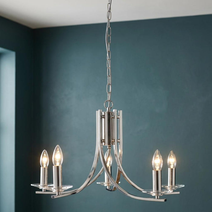 Ascona 5-light satin silver chandelier with glass sconces and lit candle bulbs against a teal wall.