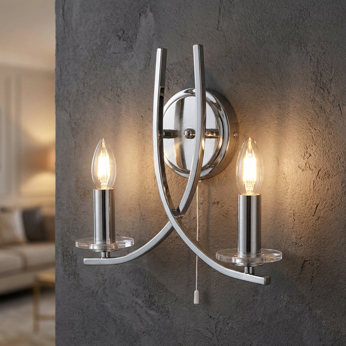 Ascona two-light satin silver wall sconce with curved arms and clear glass discs on a dark textured wall.