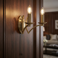 Antique brass wall light with two glowing candle bulbs and a pull cord mounted on a dark wood-paneled wall.