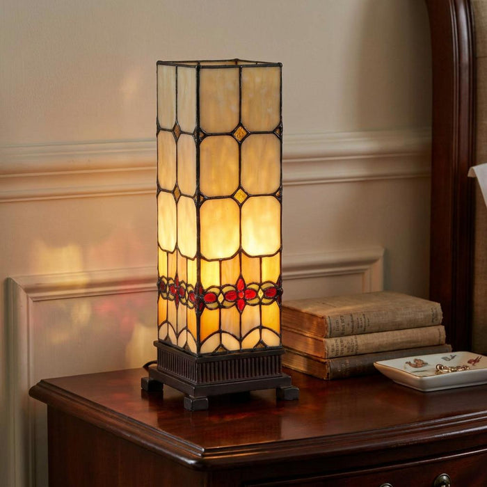 Tall square Tiffany-style table lamp with warm stained glass and red floral details on a dark wood nightstand.