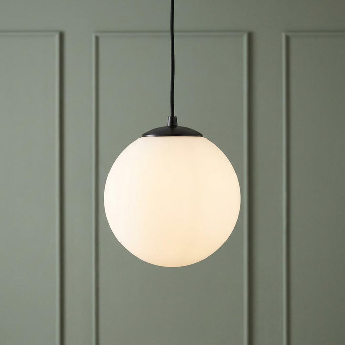 Opal glass sphere pendant light glowing against a sage green paneled wall.