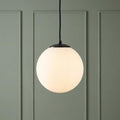 Opal glass sphere pendant light glowing against a sage green paneled wall.