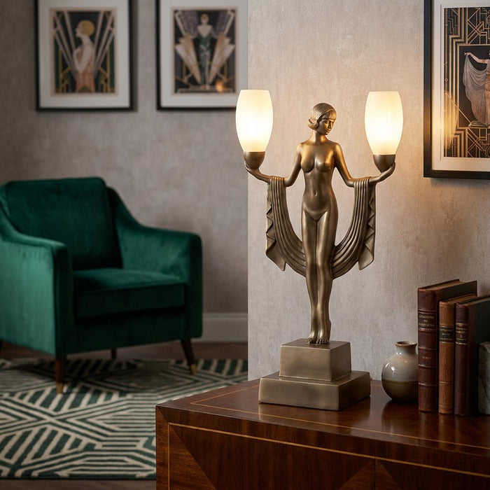 Bronze Art Deco table lamp featuring a female figure holding two frosted glass shades, set in a vintage living room.