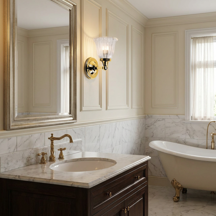 Polished brass wall light with a fluted cloche shade mounted on a paneled wall in a traditional marble bathroom.