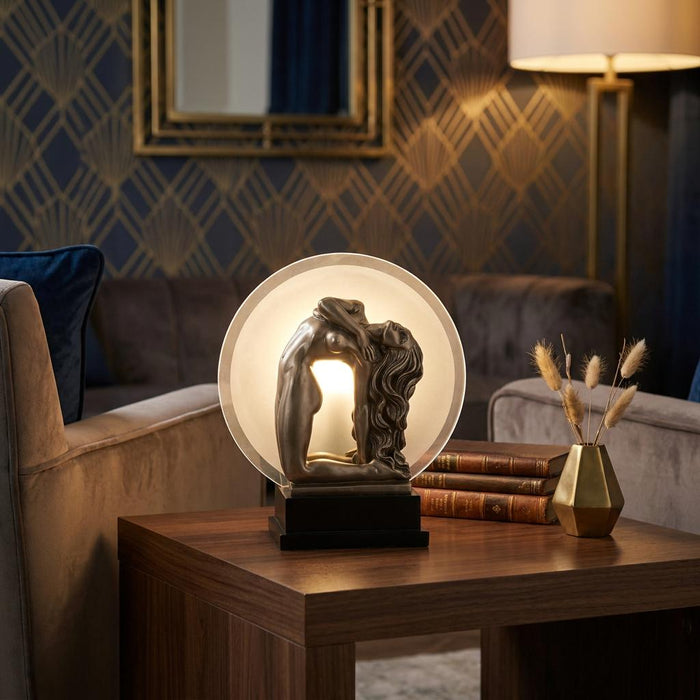 Awakening Art Deco figurine lamp on a wooden table, featuring a metallic female figure silhouetted against a glass disc.