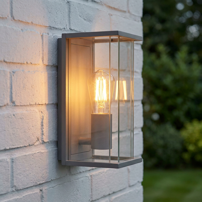 Grey rectangular boxed outdoor wall light with an illuminated filament bulb on a white brick wall.