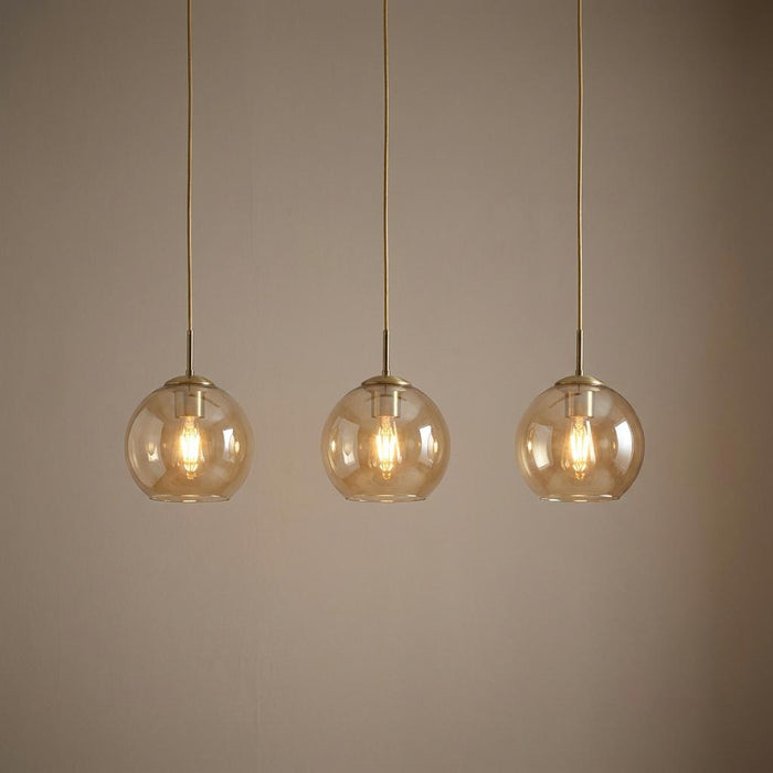 Trio of amber glass globe pendant lights with brass hardware hanging against a neutral wall.